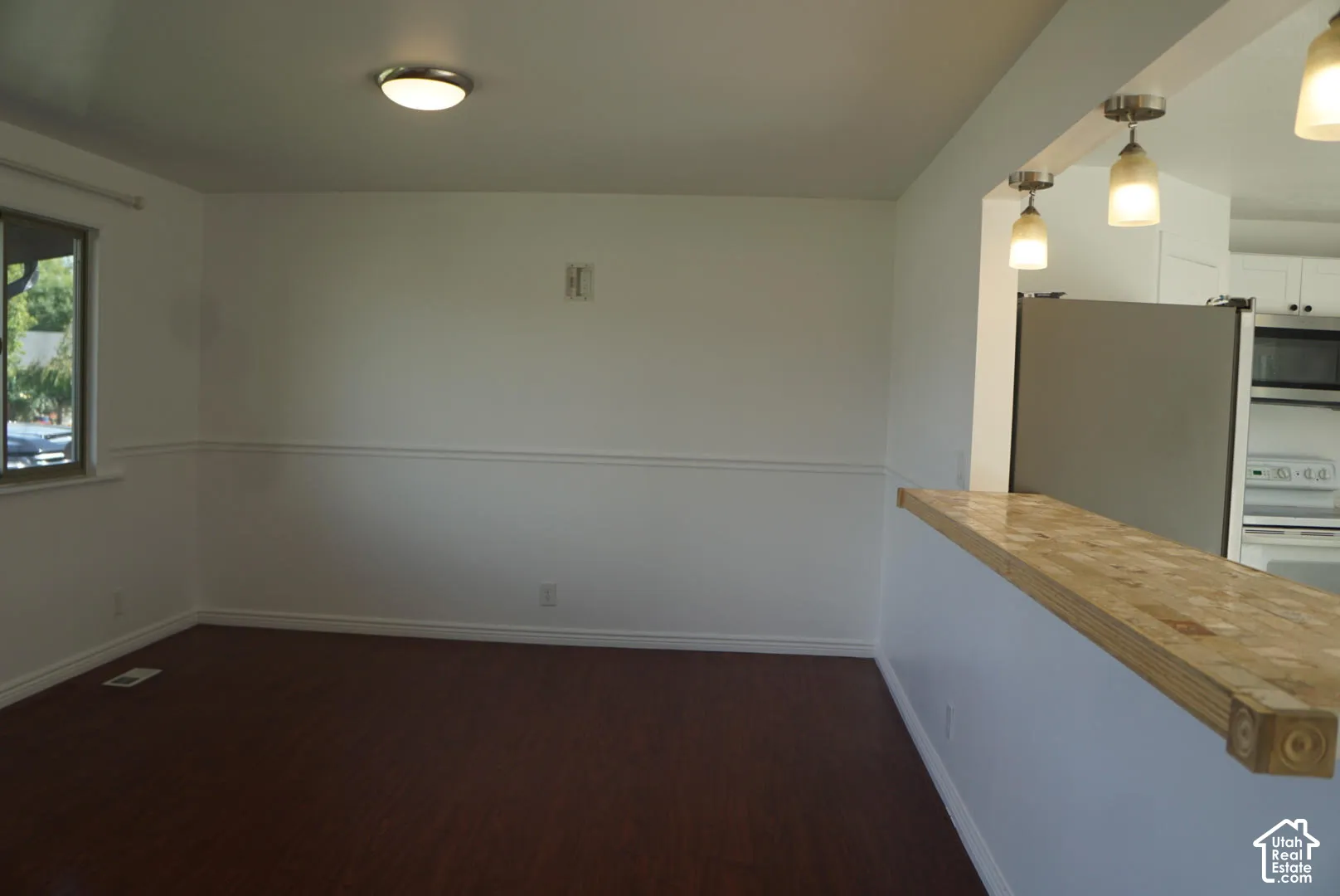 Wood-finish flooring, chair rail molding, ceiling-mounted light fixture, and stone-topped breakfast bar with dual pendant lighting