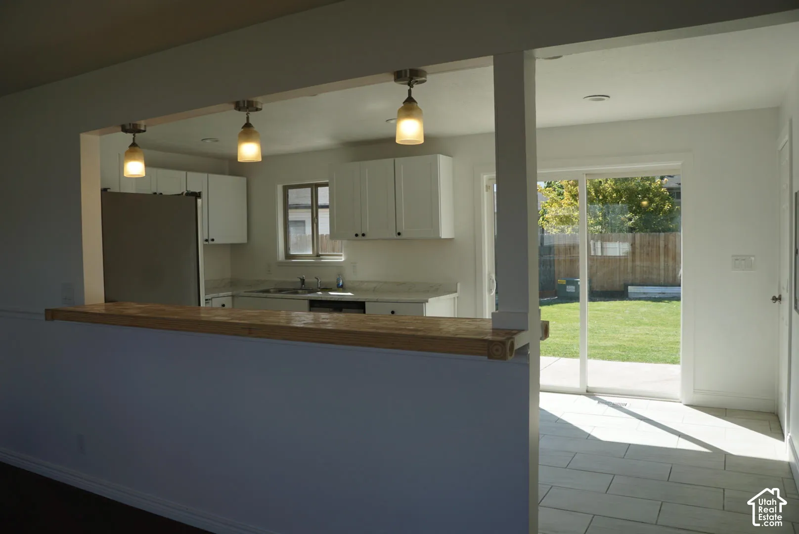 Kitchen featuring white cabinetry, stone-finish countertops, a wood-topped breakfast bar, three pendant lights, and glass sliding doors
