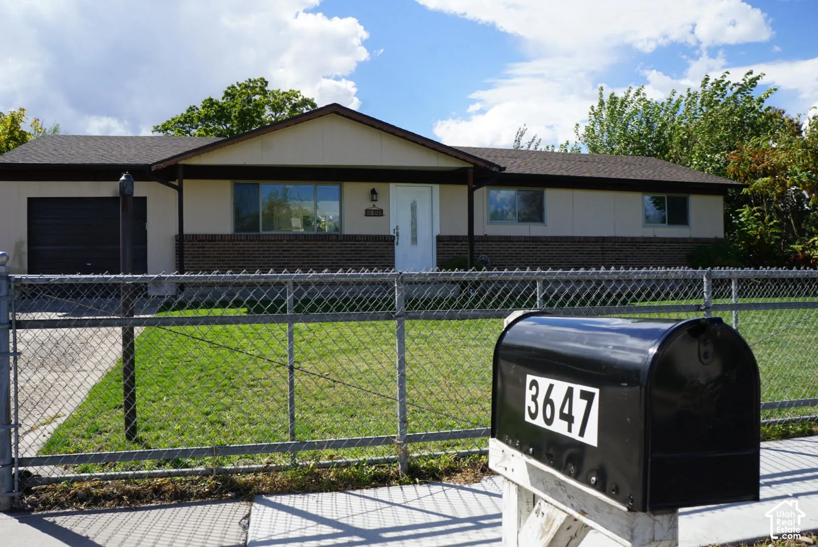 Single-story exterior featuring a brick and panel facade, asphalt shingle roof, attached garage, and a chain-link fence