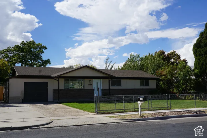 Single-story ranch-style exterior featuring a brick and stucco facade, asphalt shingle roof, attached garage, and chain-link fenced yard