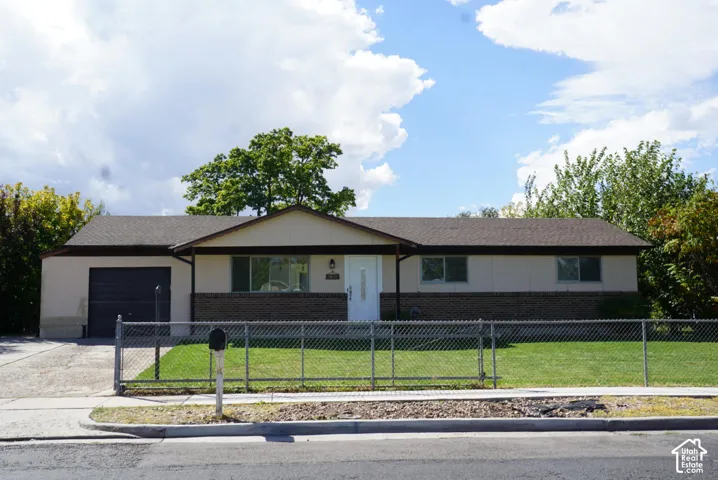 Single-story residence featuring a brick and siding exterior, asphalt shingle roof, attached garage, and chain-link fenced yard