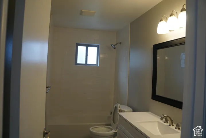 Bathroom featuring a white vanity with an integrated basin, a three-light vanity fixture, a framed wall mirror, and a tub-shower combination with tiled surround
