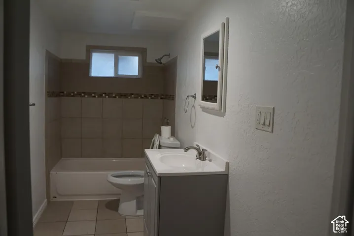 Bathroom featuring a grey vanity with an integrated sink, tiled bathtub surround with a decorative accent border, tiled flooring, and a wall-mounted mirror