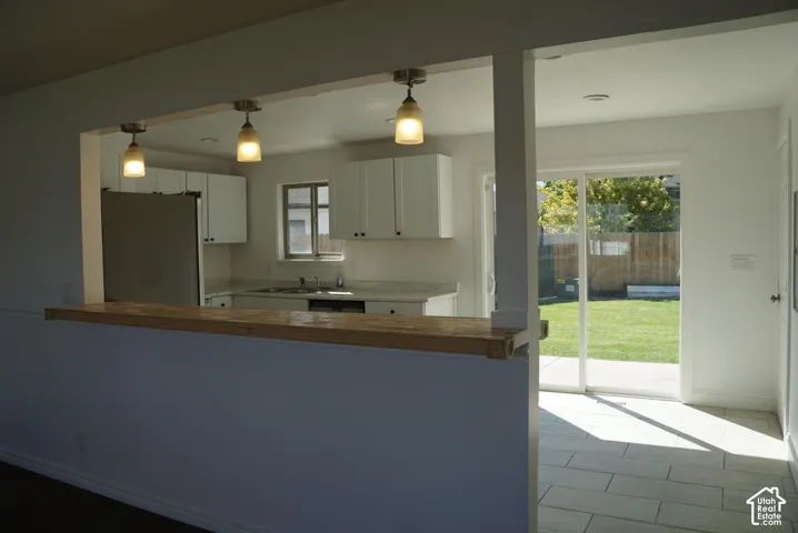 Kitchen featuring white cabinetry, stone-finish countertops, a wood-topped breakfast bar, three pendant lights, and glass sliding doors