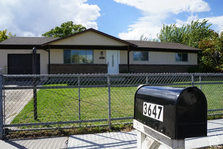 Single-story exterior featuring a brick and panel facade, asphalt shingle roof, attached garage, and a chain-link fence