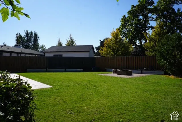 Backyard featuring a grass lawn, full-perimeter wood fencing, concrete patio space, and a stone-encased fire pit
