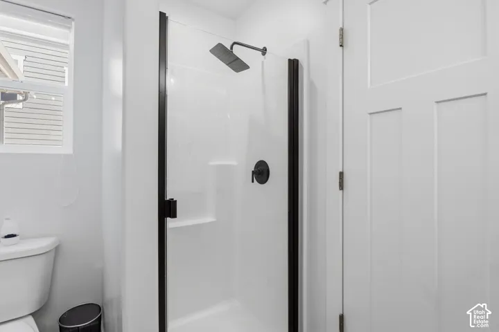 Walk-in shower featuring a white surround, matte black hardware, and a glass door with a black frame