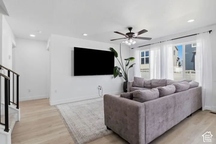 Living area featuring wood-finish flooring, recessed lighting, a ceiling fan with integrated light fixture, and multiple windows