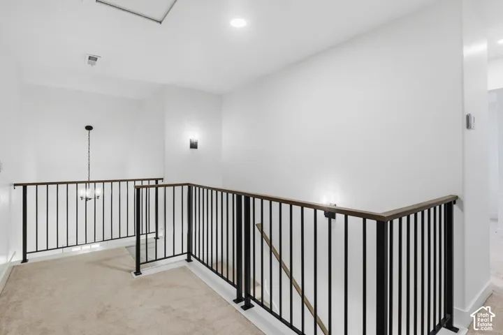 2nd floor hallways Landing area featuring neutral carpet, upgraded metal baluster railing, wood-finish handrails, and wall-mounted light fixtures.
