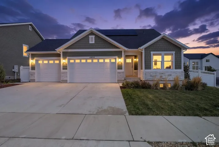 Welcoming ranch-style home featuring a two-car garage with paneled doors, stone and fiber cement exterior detailing, and illuminated architectural accents