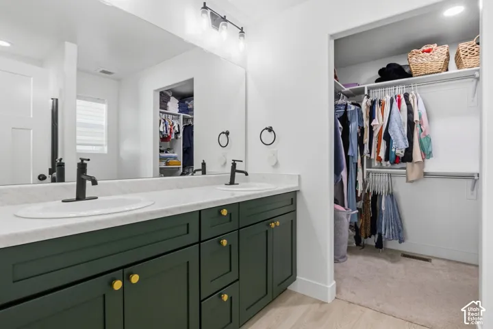 Dual-sink vanity featuring dark green Shaker-style cabinetry, gold-tone hardware, stone-finish countertops, and matte black plumbing fixtures. Walk-in closet