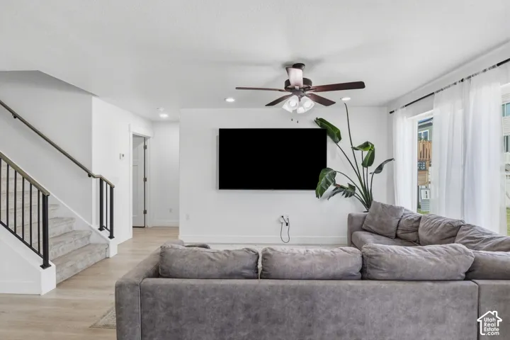Interior space featuring light wood-finish flooring, recessed lighting, ceiling fan with integrated light fixture, and staircase with black metal balusters and wooden handrail