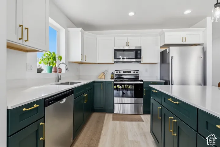 Kitchen featuring two-tone cabinetry with brass-finish hardware, quartz countertops, stainless steel appliances, and wood-finish flooring