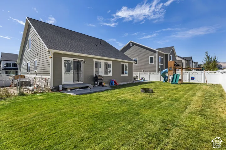 Rear exterior featuring horizontal lap siding, stone veneer accents, sliding glass door, and a fenced-in yard with a paved patio