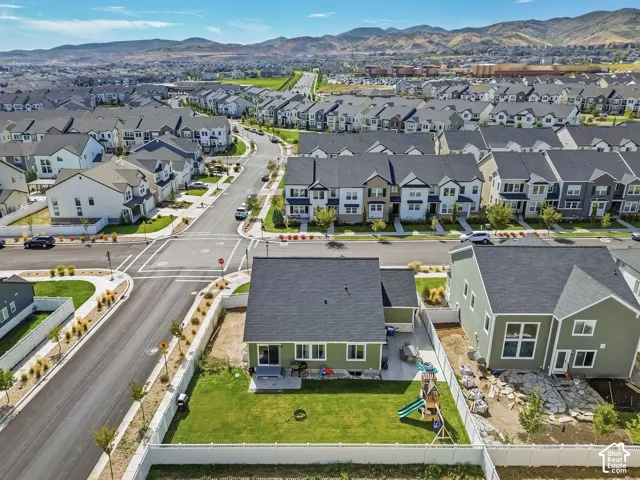 Aerial perspective of a corner-lot property featuring a fenced backyard, a concrete patio, a manicured lawn, and mountain scenery