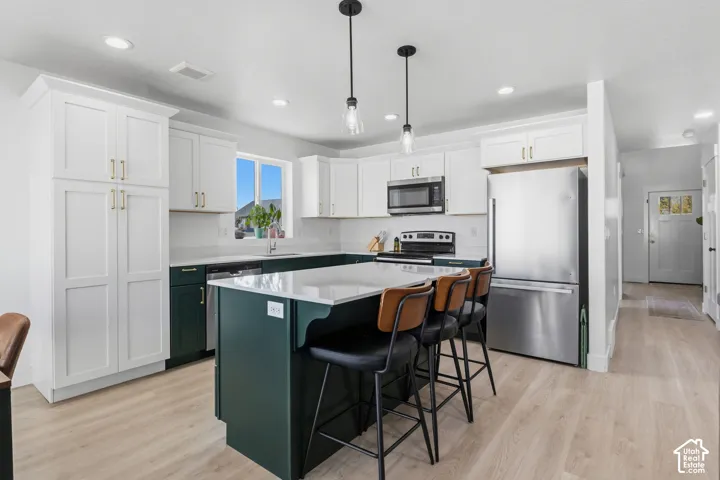 Kitchen featuring two-tone cabinetry, central island with light-toned quartz countertop, stainless steel appliances, pendant lighting, and wood-finish flooring