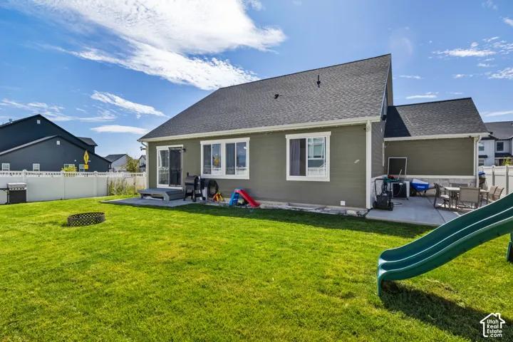 Rear exterior featuring green horizontal siding, asphalt shingle roofing, concrete patio, and white vinyl privacy fencing