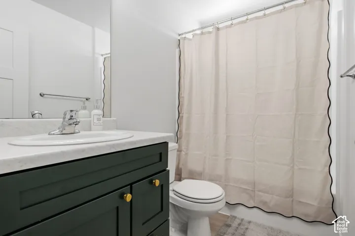Main level full bathroom vanity featuring dark-toned cabinetry, gold-tone hardware, a white stone-look countertop with an integrated basin, and a wall-to-wall mirror