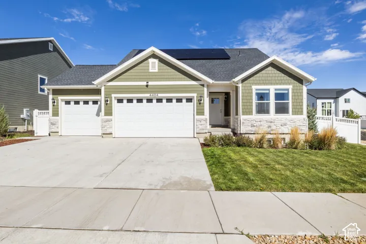 Single-story exterior featuring fiber-cement shingle siding, stone veneer accents, a three-car garage, and roof-mounted solar panels