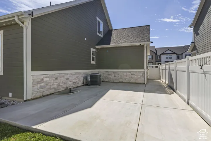 Concrete patio exterior featuring horizontal lap siding, stone veneer accents, and white vinyl privacy fencing