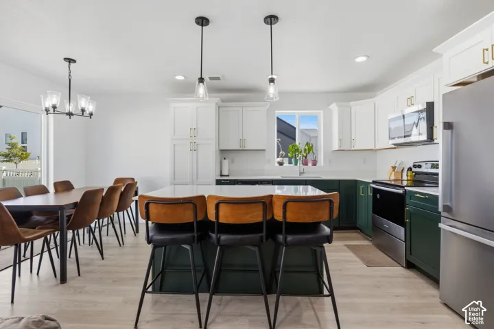 Kitchen featuring a central island with a solid-surface countertop, two-tone cabinetry, stainless steel appliances, and wood-finish flooring