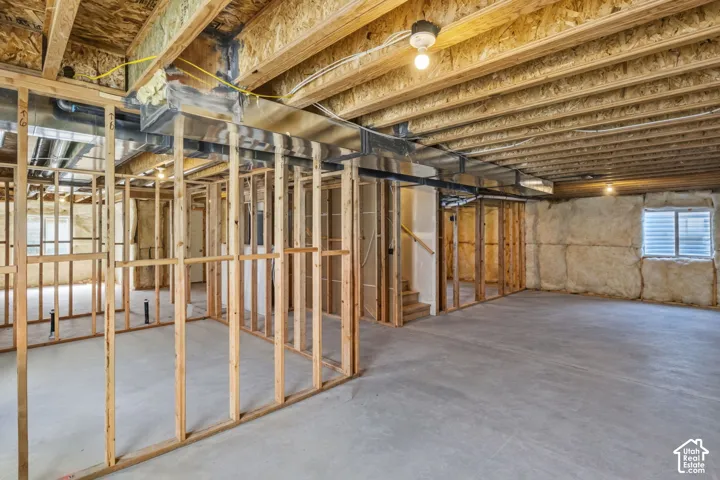 Unfinished basement level featuring exposed wood framing, concrete foundation walls with insulation, concrete flooring, metal ductwork, and an egress window