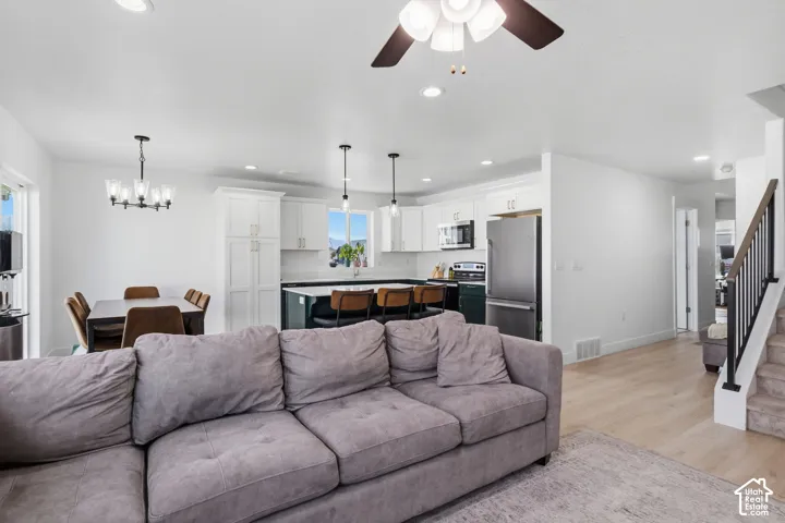 Kitchen featuring white upper cabinetry, dark base cabinetry, a center island with pendant lighting, recessed ceiling lights, and light wood-finish flooring
