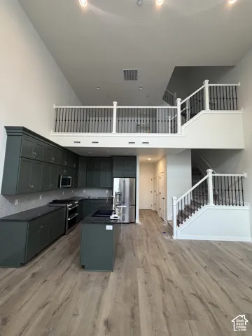 Kitchen featuring floor-to-ceiling dark cabinetry, stone countertops, stainless steel appliances, wood-finish flooring, and a two-story ceiling with a railed loft balcony
