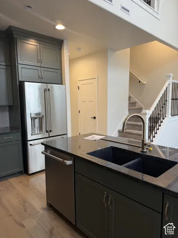 Kitchen featuring dark-toned cabinetry, stainless steel appliances, a dark stone countertop, a dual-basin sink with a gooseneck faucet, and wood-finish flooring