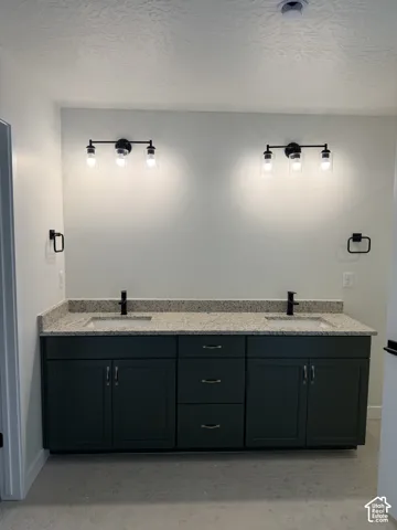 Dual-sink vanity featuring charcoal-colored cabinetry, stone-composite countertop with integrated basins, matte black fixtures, and double wall-mounted light bar hardware
