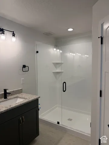 Bathroom featuring a vanity with dark cabinetry, stone-finish countertop, undermount sink, and matte black hardware, paired with a glass-enclosed shower featuring built-in corner shelving