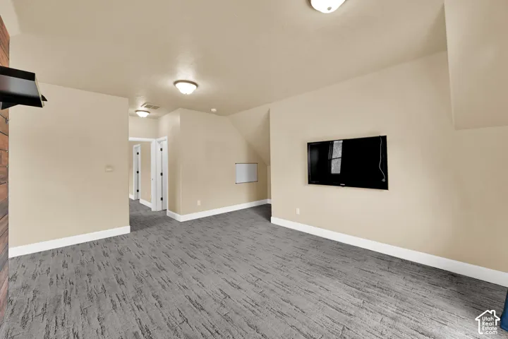 Neutral-toned interior space featuring textured wall-to-wall carpeting, recessed and surface-mounted lighting, and a wood-paneled accent wall
