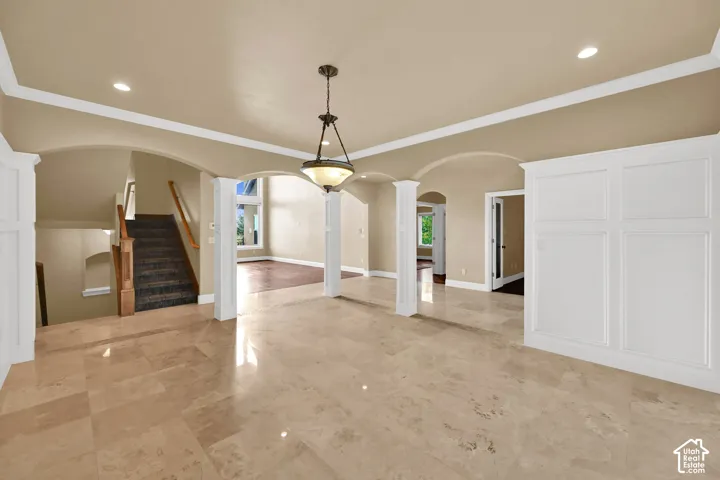 Stone tile flooring, recessed lighting, arched architectural openings with decorative columns, crown molding, and wall paneling