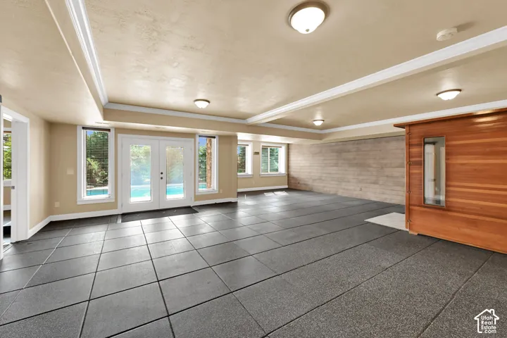 Spacious room featuring rubber tile flooring, (removable with herringbone patterned tile underneath)  double glass-paneled doors, recessed ceiling lighting, a textured accent wall, and a built-in wood-paneled sauna