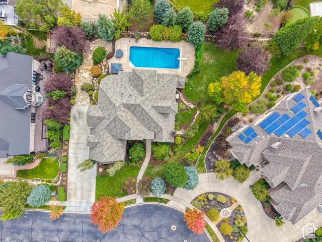 Aerial perspective of a multi-gabled roofline residence featuring an inground swimming pool, concrete hardscaping, extensive mature landscaping, and a multi-car driveway