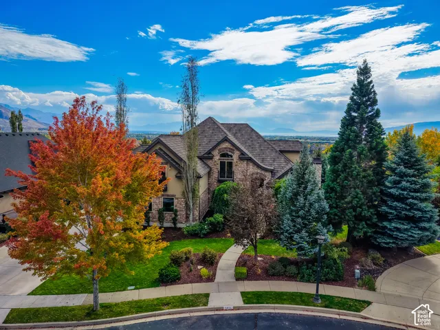Multi-level residential exterior featuring stone veneer facade, metal roofing, integrated balcony, and manicured landscaping with mature trees