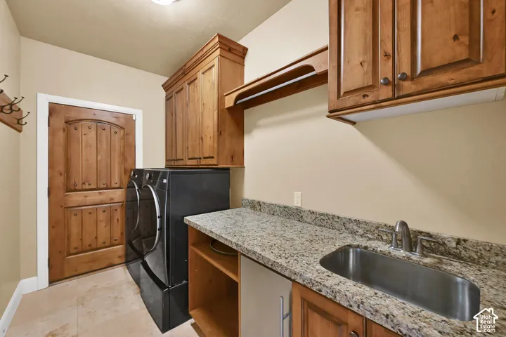 Utility room featuring custom wood cabinetry, stone-surface countertops, an undermount stainless steel sink with a high-arch faucet, and a paneled wood door