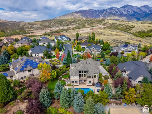 Aerial perspective of a multi-story residence featuring a private swimming pool, stone-patterned exterior, steep-pitched rooflines, and mountain scenery