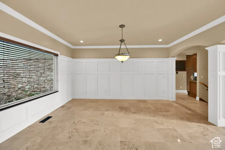 Dining area featuring extensive white wainscoting, large-format tile flooring, crown molding, and a tiered pendant light fixture