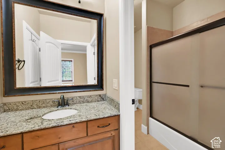 Bathroom featuring a vanity with stone-finish countertop, undermount sink, dark-framed wall mirror, and tub-shower combination with sliding glass doors
