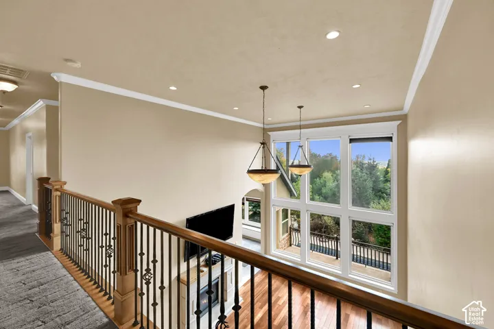 Interior walkway featuring a wood and wrought-iron railing, two tiered-style pendant light fixtures, recessed ceiling lighting, and floor-to-ceiling windows