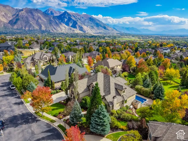 Aerial perspective of a multi-gabled residence featuring stone and stucco exterior cladding, an attached multi-car garage, a backyard swimming pool, and professional landscaping set against a prominent mountain backdrop