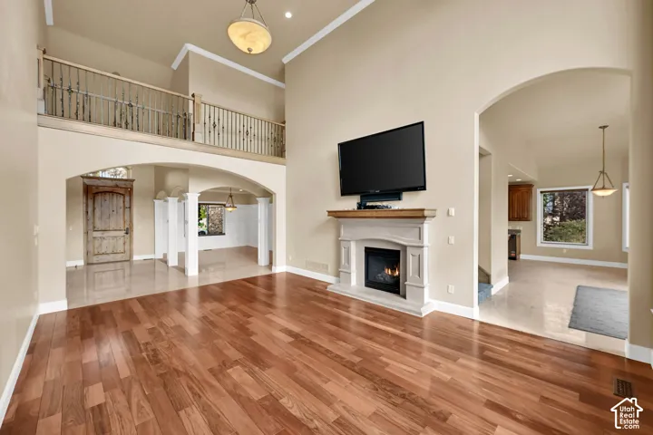 Two-story volume ceiling featuring a wrought iron railing, wood-finish flooring, a stone-surround fireplace with a wooden mantel, and decorative arched architectural details