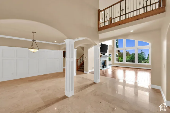 Interior space featuring polished stone flooring, custom wainscoting, arched architectural detailing, a multi-story balcony with metal railings, and a two-story window wall