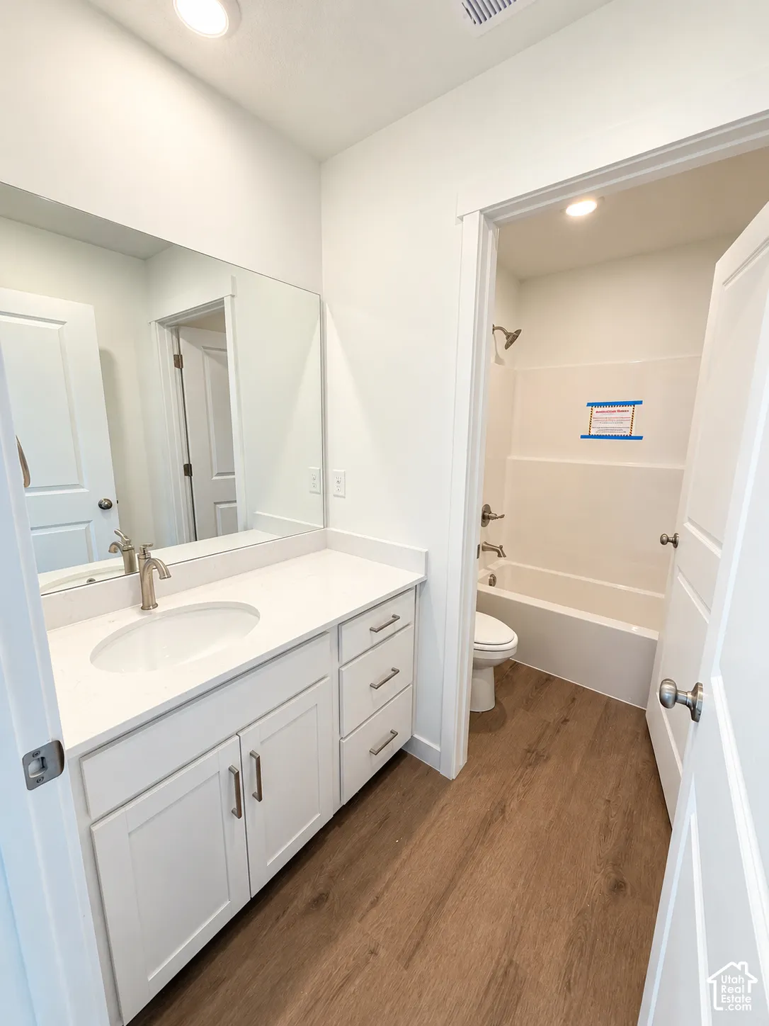 White vanity cabinetry with a stone-surface countertop, an oval undermount sink, brushed nickel hardware, and wood-finish flooring