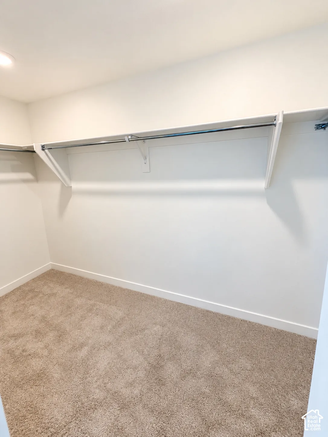 Walk-in closet featuring plush wall-to-wall carpeting and built-in white shelving with a metal garment rod