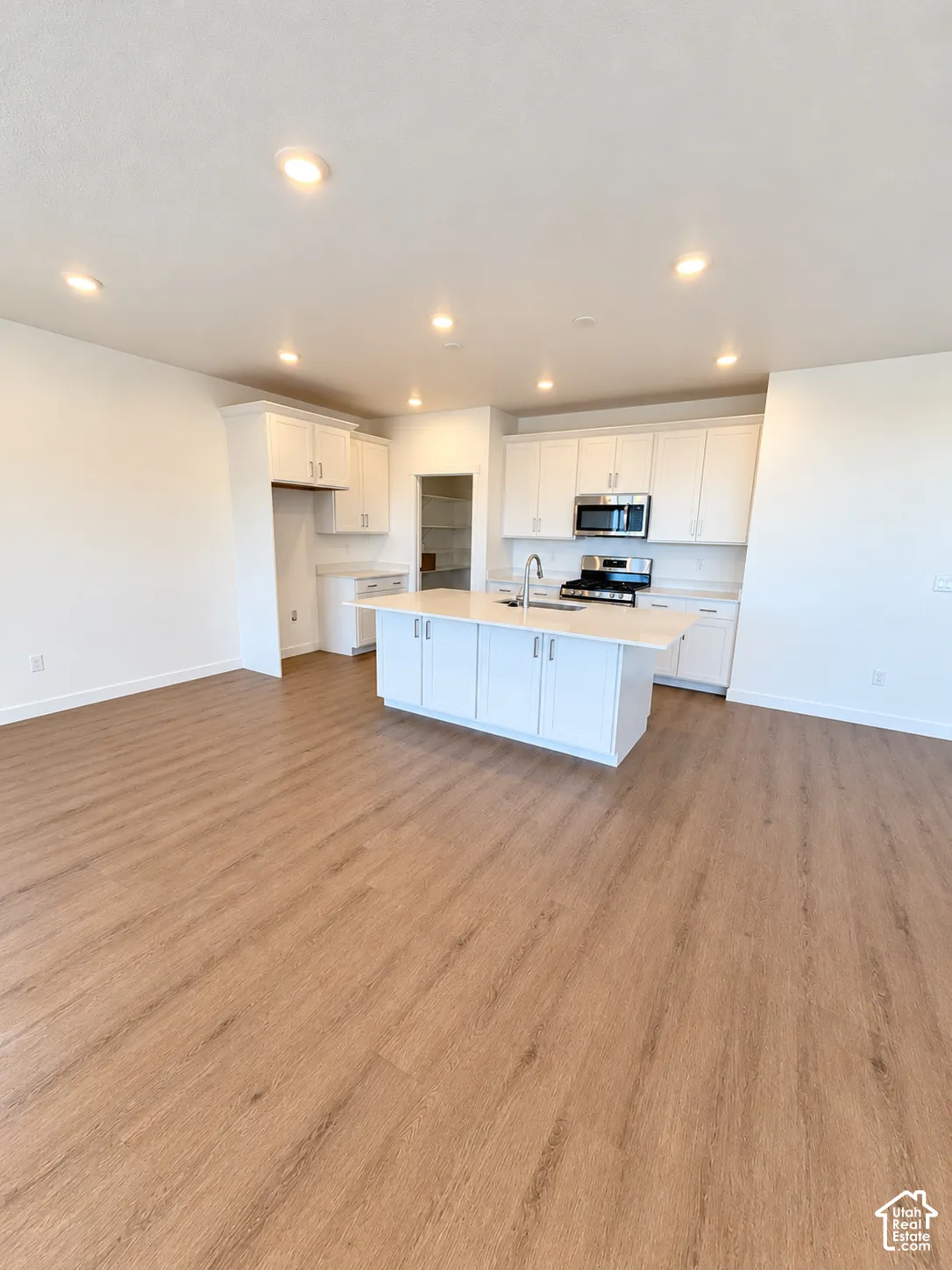 Kitchen featuring white shaker-style cabinetry, quartz countertops, a central island with an integrated sink, stainless steel appliances, and wood-finish flooring