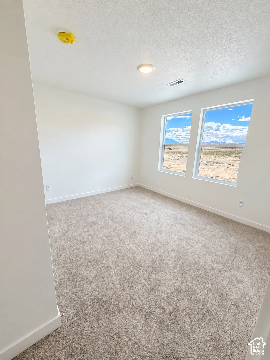 Neutral interior featuring wall-to-wall carpeting, crisp white walls, and dual windows showcasing an expansive desert horizon