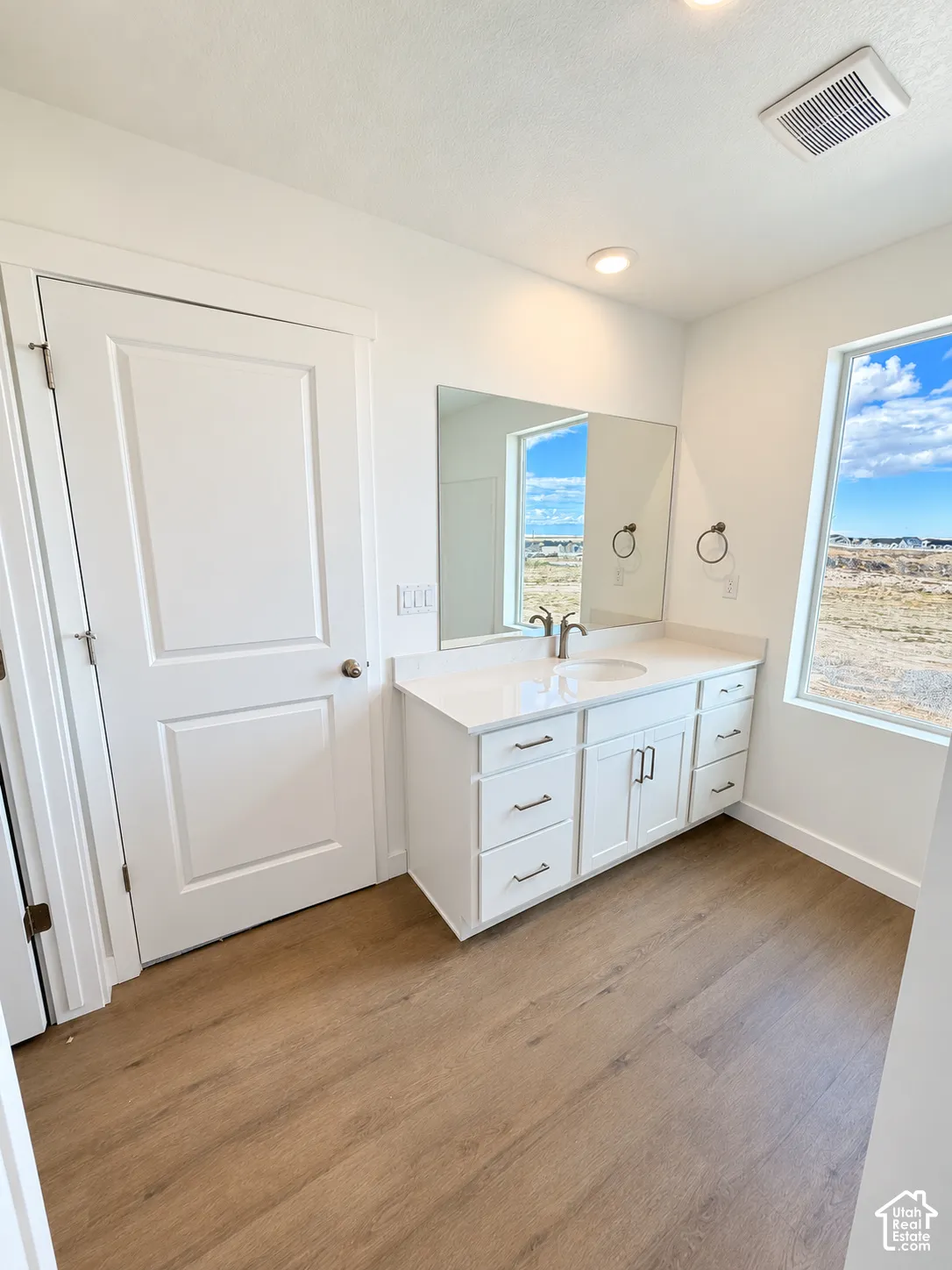 White vanity featuring a solid surface countertop, undermount sink, multi-drawer storage, and wood-finish flooring