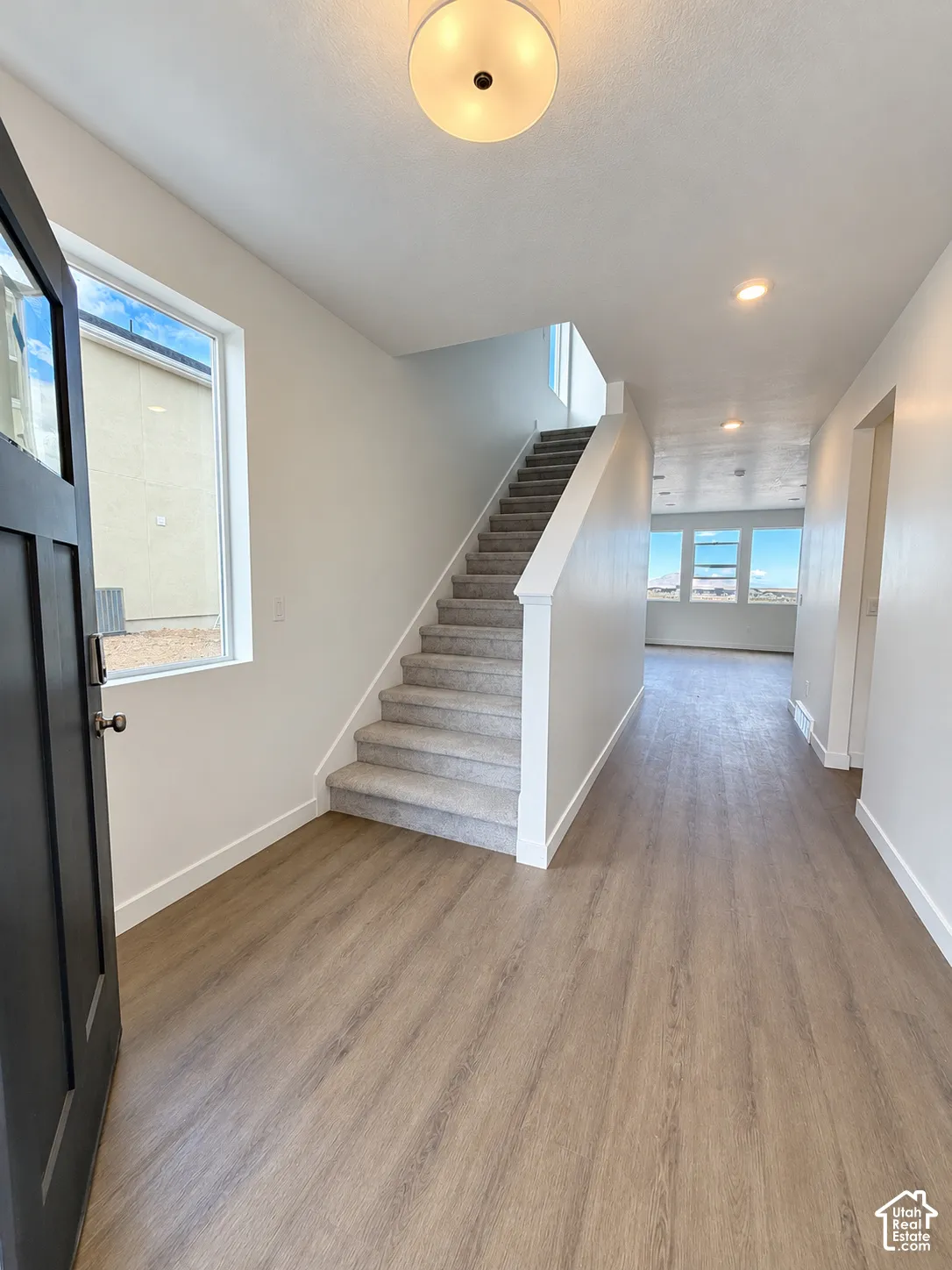Entryway featuring wood-finish flooring, a dark-toned door with a glass pane, carpeted stairs, and a circular flush-mount ceiling light fixture